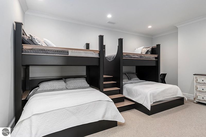 This interior shot showcases a bedroom featuring two sets of bunk beds, designed with a modern aesthetic. The beds are dark-colored with light wood accents, complemented by neutral bedding and pillows. The room is well-lit and appears spacious, making it ideal for a children's room or guest bedroom.