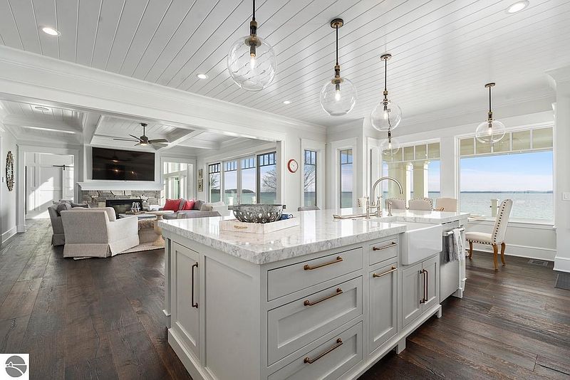 This interior shot showcases a bright, open-concept kitchen and living area. The kitchen features a large island with marble countertops, custom cabinetry, and pendant lighting. The adjacent living room includes a fireplace and comfortable seating, creating an inviting and luxurious space.