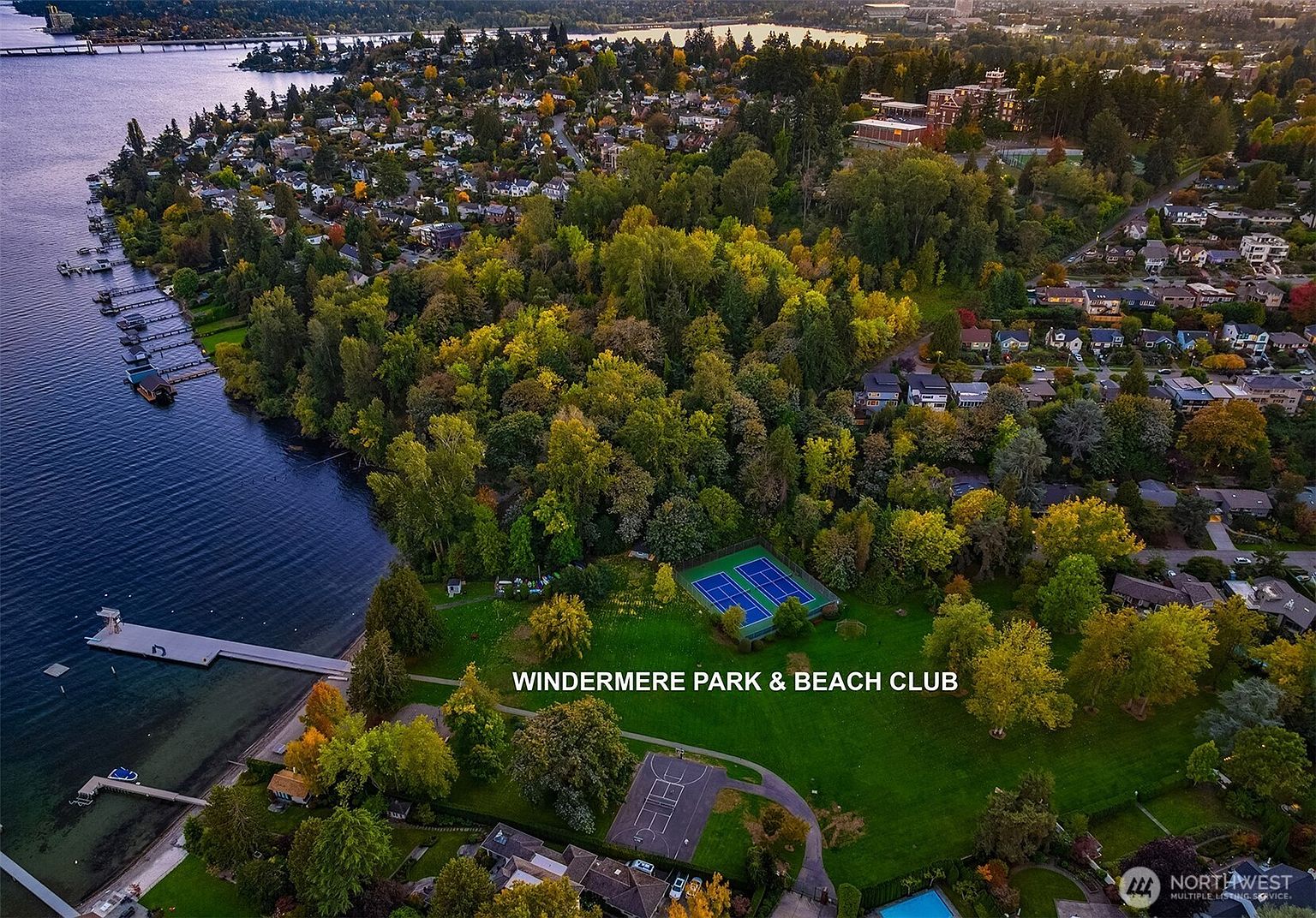 This is an aerial view of Windermere Park & Beach Club, showcasing its lush green spaces, tennis courts, basketball court, and proximity to the water. The image highlights the community's recreational amenities and desirable location, emphasizing the lifestyle benefits for potential residents. The perspective is from above, providing a comprehensive view of the park's layout and surrounding neighborhood.