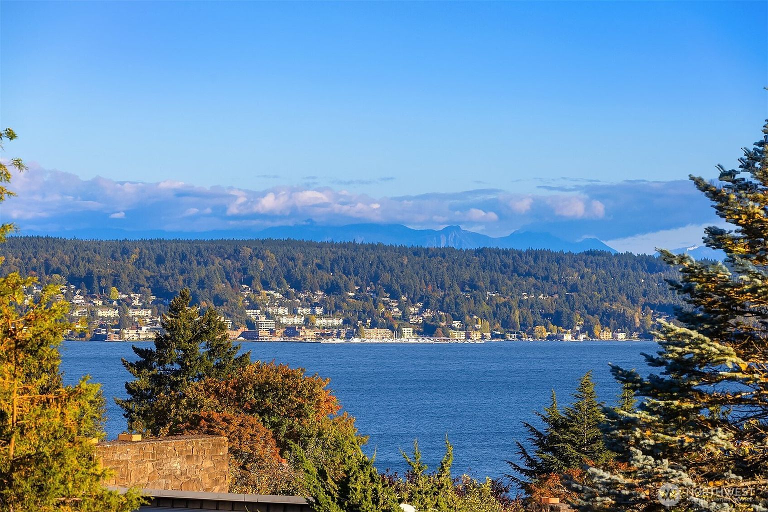 This picturesque exterior shot showcases a stunning view of a serene body of water, framed by lush greenery and distant mountains under a clear blue sky. The scene evokes a sense of tranquility and natural beauty, highlighting the property's desirable location and scenic surroundings. The perspective is from an elevated position, offering a wide and immersive view.