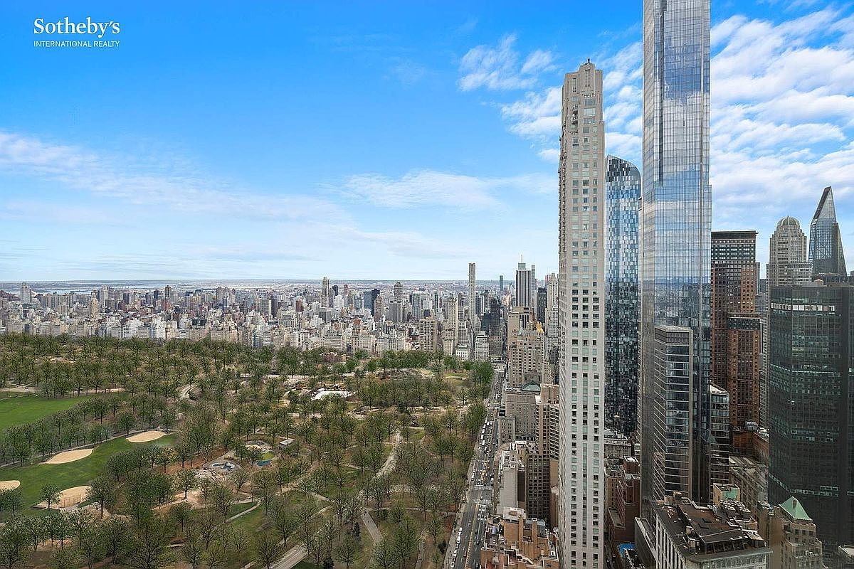 This high-altitude aerial view captures a breathtaking perspective of Central Park and the surrounding Manhattan skyline. The composition highlights the contrast between the lush greenery of the park and the dense, towering skyscrapers that define the city's iconic architecture. The clear blue sky and expansive horizon emphasize the prestige and prime location of this luxury vantage point.