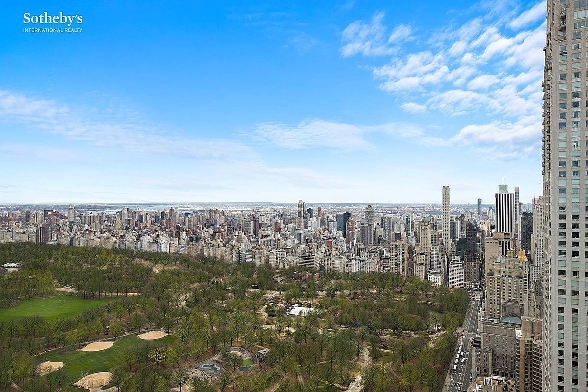 This high-altitude aerial view captures a breathtaking panoramic perspective of Central Park and the surrounding New York City skyline. The image highlights the lush greenery of the park in the foreground, transitioning into a dense, iconic urban landscape of skyscrapers under a clear blue sky. The perspective emphasizes the prestigious location and the expansive, unobstructed views offered by the property.