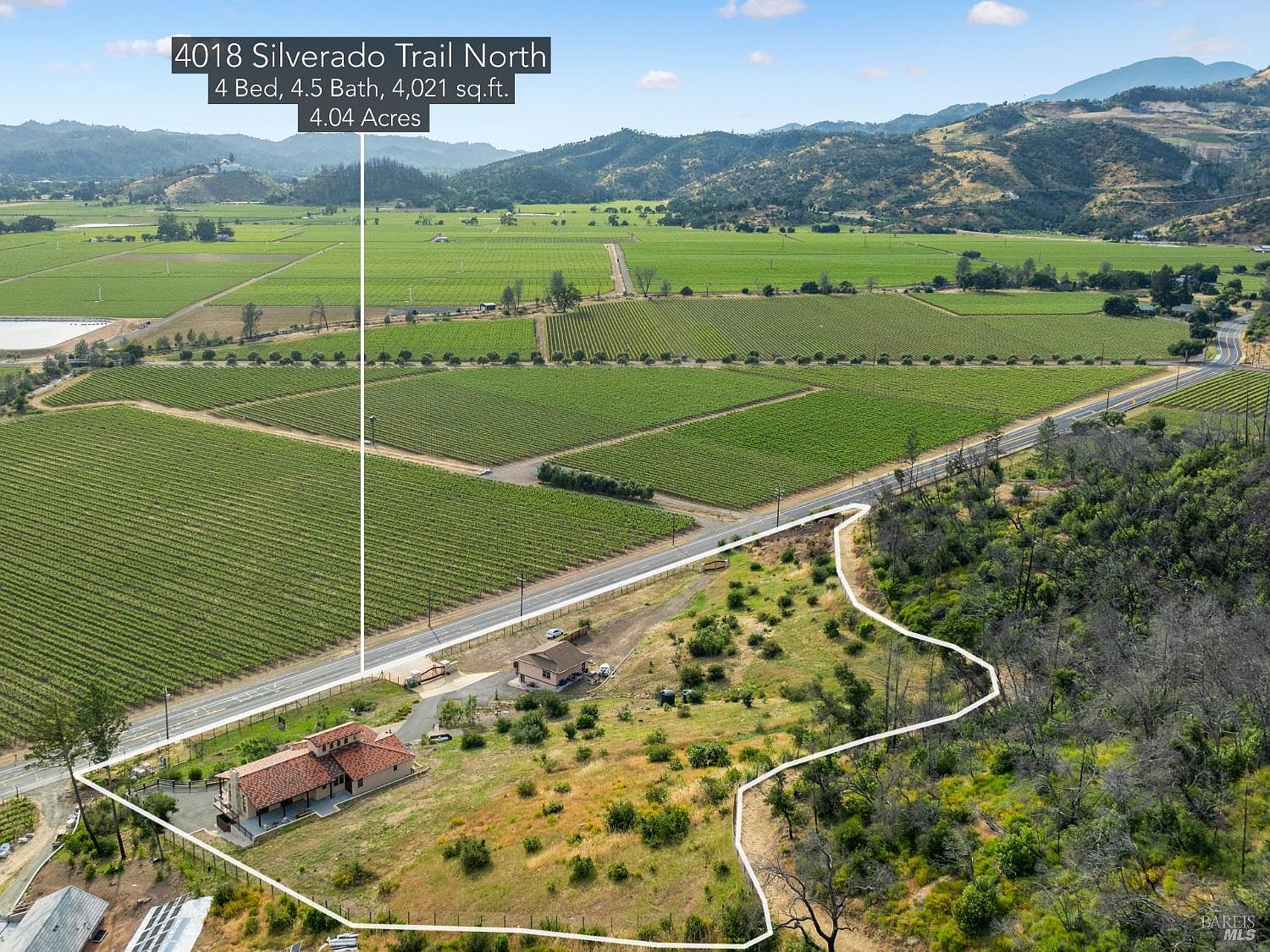 This aerial view showcases a property with a vineyard, a residential building with a red tile roof, and surrounding land. The property is bordered by a road and features a mix of cultivated land and natural vegetation. The image provides a comprehensive overview of the property's layout and its integration with the surrounding landscape, emphasizing its size and location.