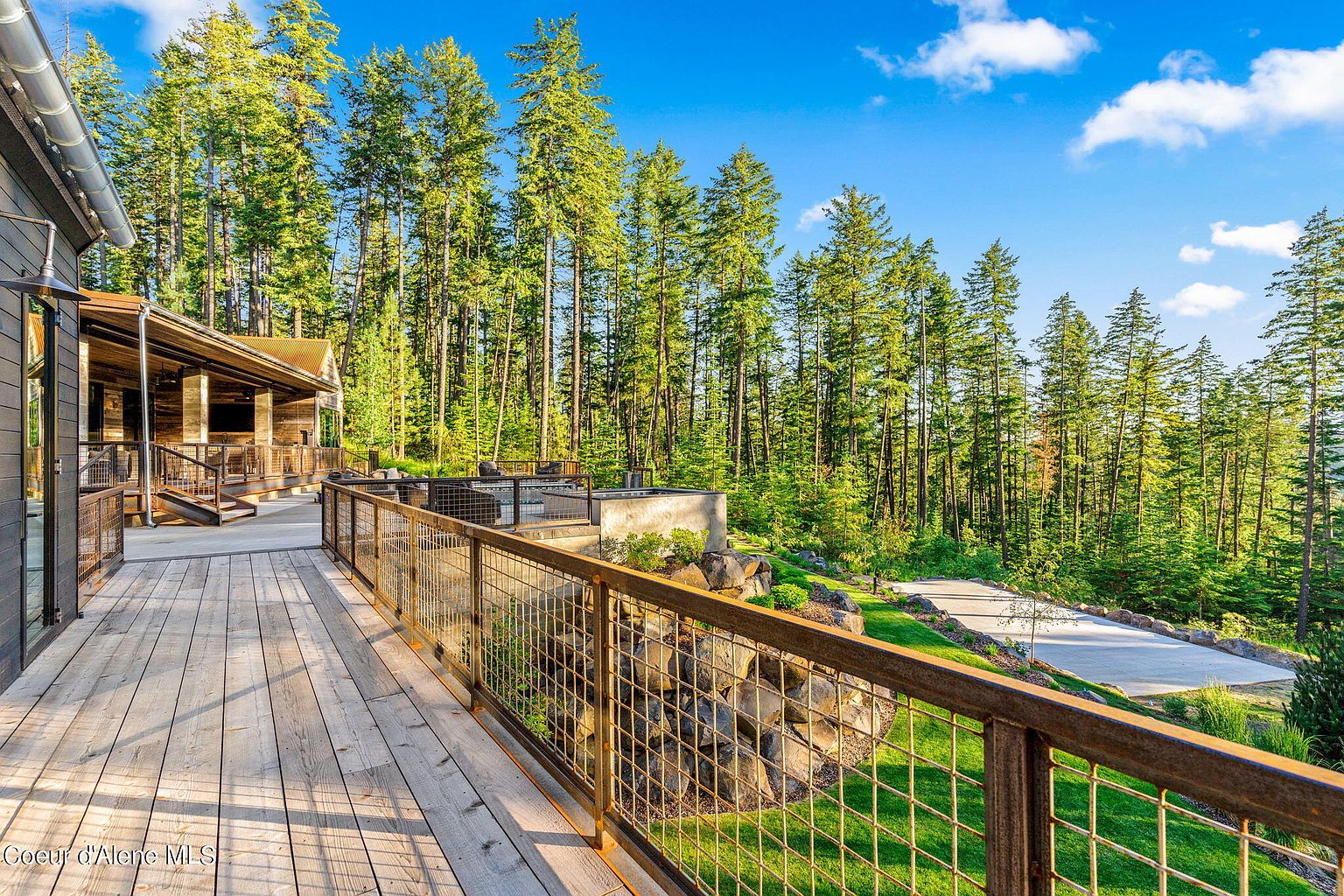 This image showcases a spacious wooden deck with a metal railing, offering an inviting outdoor living space. The deck overlooks a lush green lawn and a dense forest, creating a serene and private atmosphere. The design seamlessly blends with the natural surroundings, enhancing the property's appeal.