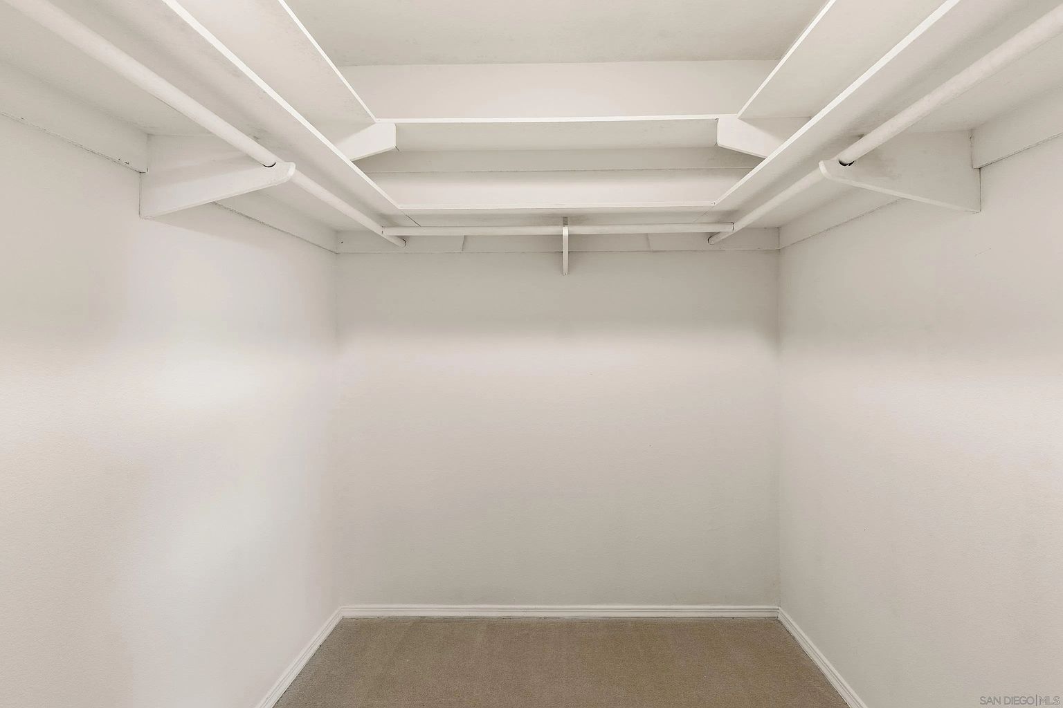 This is a walk-in closet featuring white walls, carpeted flooring, and built-in shelving and hanging rods. The closet is empty, providing a blank canvas for potential buyers to envision their storage solutions. The space appears clean and well-maintained, offering ample room for clothes and accessories.