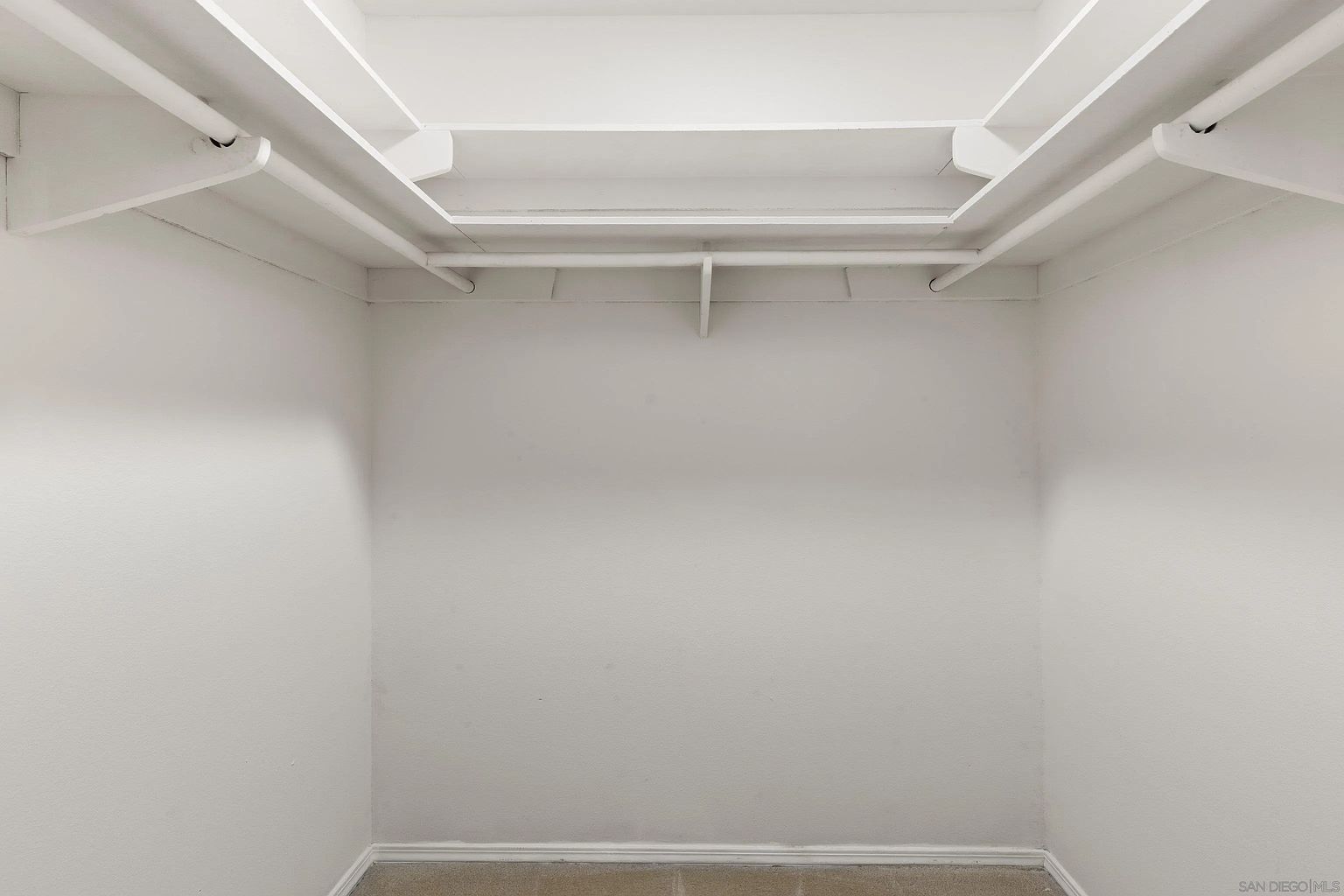 This is a walk-in closet featuring white walls and built-in shelving and rods. The closet appears to be empty and ready for use. The space is well-lit and clean, offering ample storage potential.