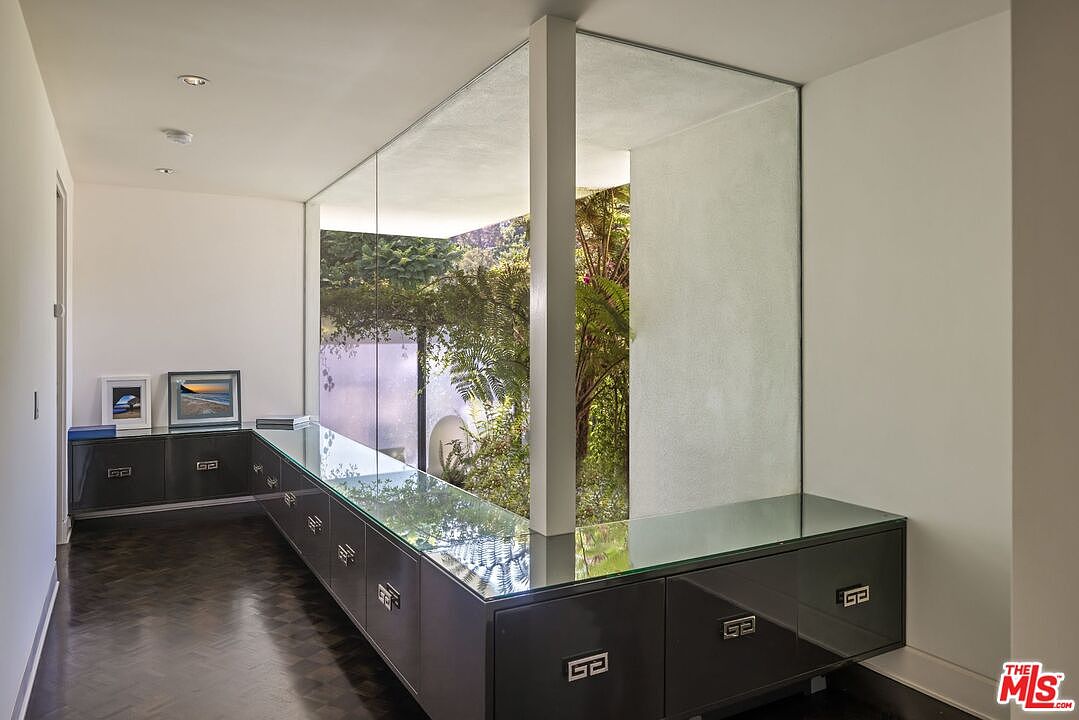 This interior shot showcases a modern hallway featuring dark wood flooring and sleek, built-in cabinetry with a glass countertop. A large window provides a view of lush greenery, creating a connection to the outdoors. The design is minimalist and sophisticated, emphasizing clean lines and natural light.