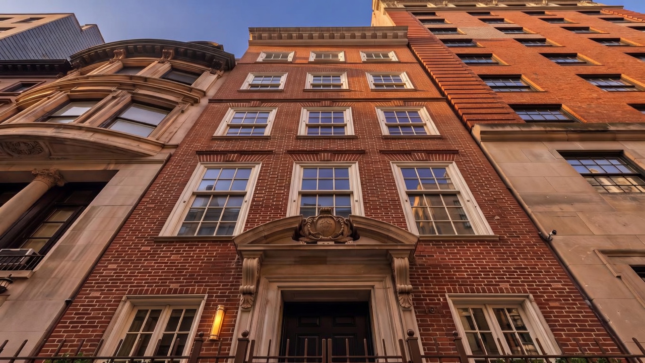 This image shows the striking front facade of a classic, multi-story brick townhouse in a dense urban setting. The architecture features symmetrical window placement, a prominent stone-surround entryway with ornate detailing, and an elevated vantage point emphasizing its height and sophisticated residential character.