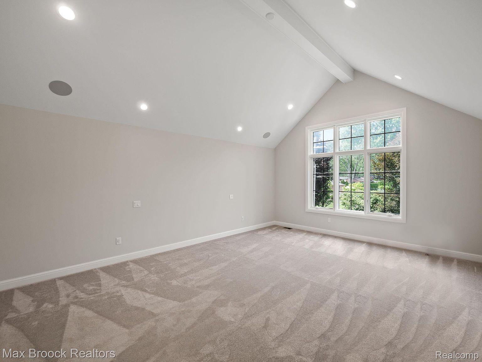 This is a spacious primary bedroom featuring neutral-toned carpet and walls, creating a serene and inviting atmosphere. A large window provides ample natural light and a view of the outdoors. The vaulted ceiling adds to the room's sense of openness and elegance, making it a desirable space for relaxation.
