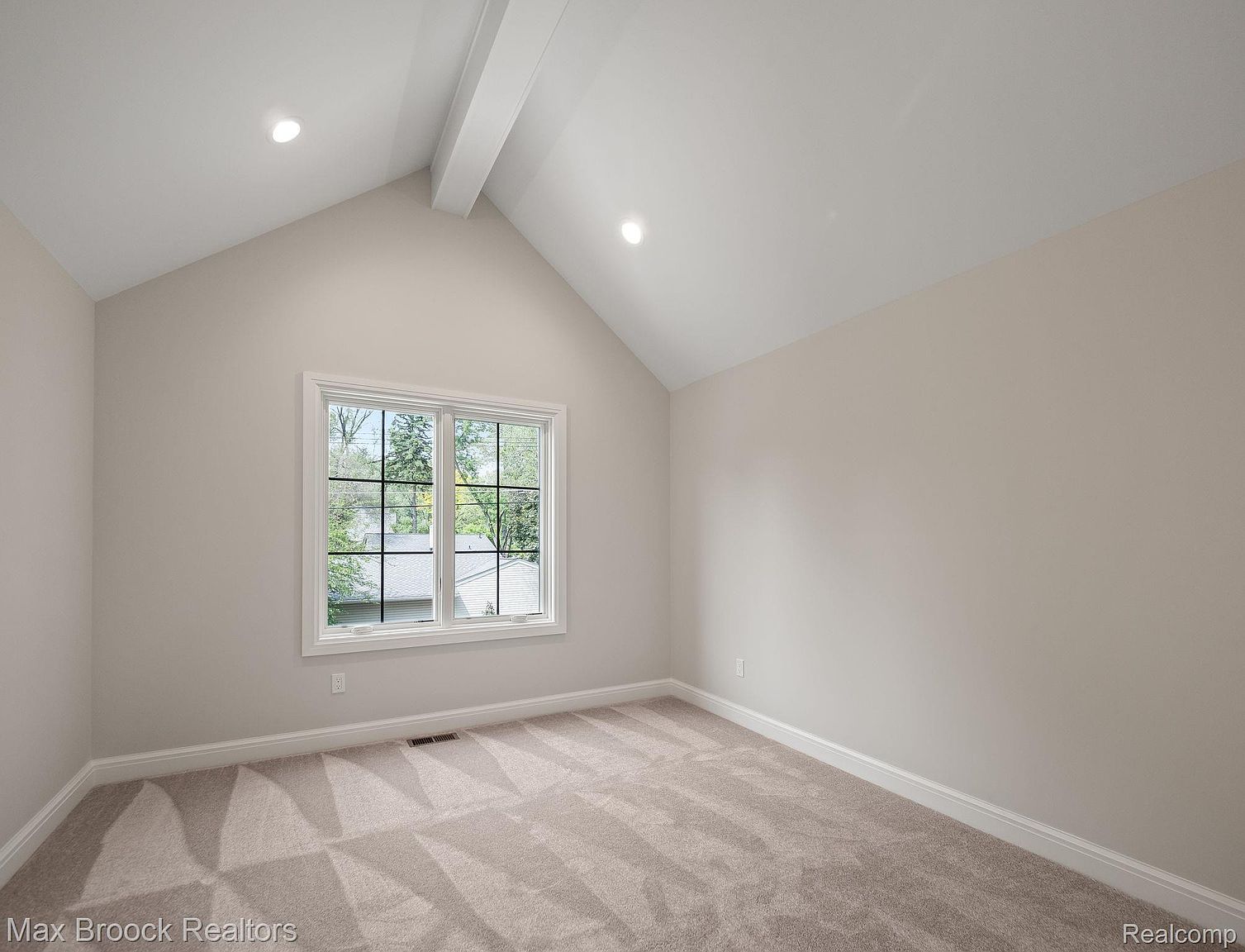 The image showcases a bright and airy bedroom with neutral-toned walls and carpet. A large window provides ample natural light and a view of the outdoors. The room features a vaulted ceiling with a beam, recessed lighting, and white trim, creating a clean and inviting space.