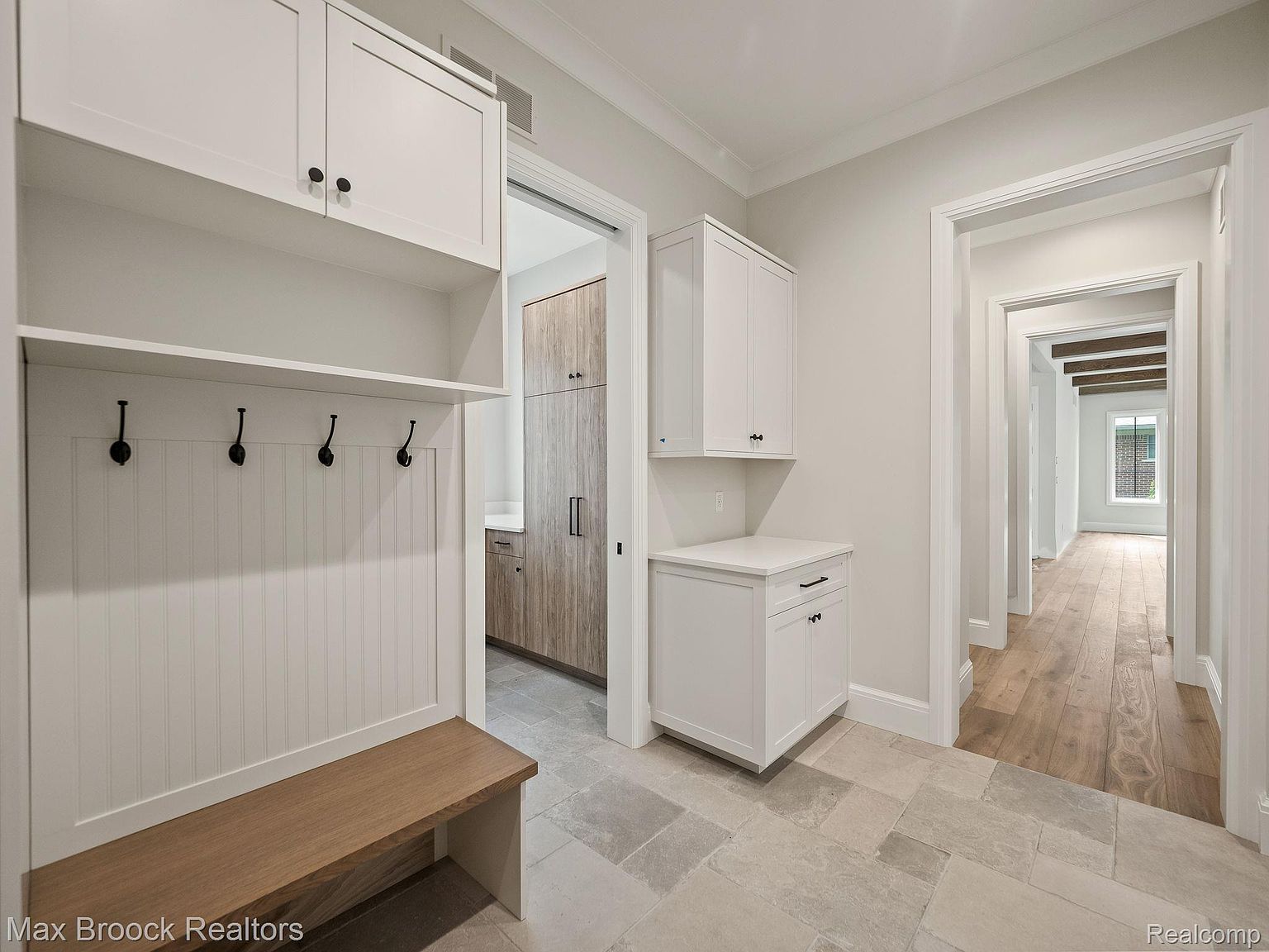 This interior shot showcases a well-lit hallway with a mudroom area featuring a built-in bench, coat hooks, and overhead cabinets. The hallway leads to other rooms, revealing hardwood flooring and neutral wall colors. The design is clean and modern, emphasizing functionality and style.