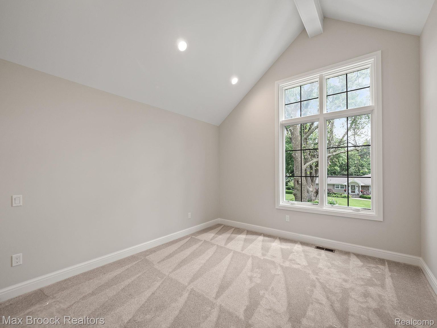 This is an interior shot of a bedroom featuring neutral-toned walls, plush carpeting, and a large window that provides ample natural light. The room has a clean and minimalist aesthetic, with a focus on creating a bright and airy space. The window offers a view of the outdoors, enhancing the room's appeal.