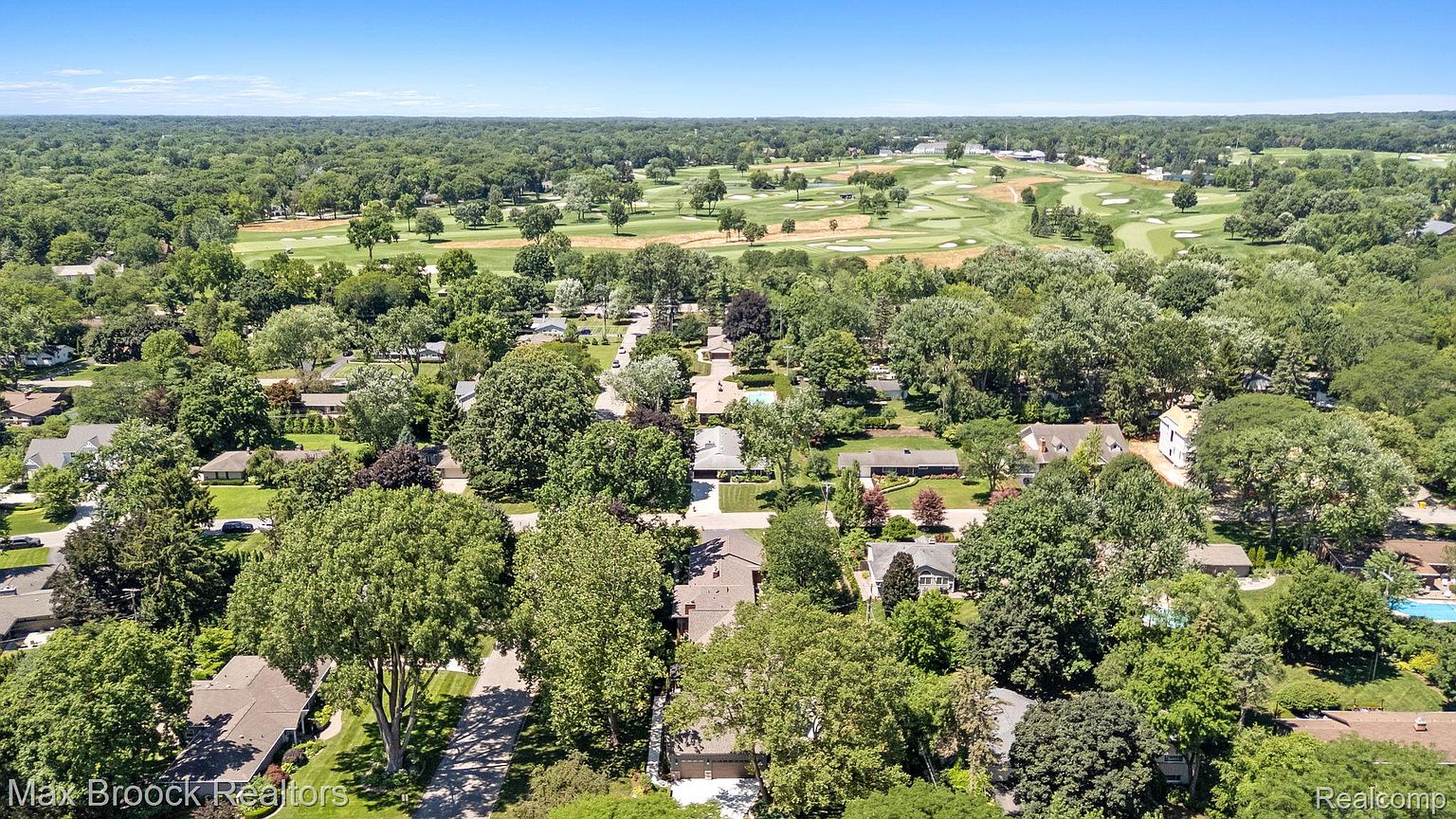This aerial shot showcases a residential neighborhood adjacent to a lush golf course under a clear blue sky. The homes are nestled among mature trees, offering a sense of privacy and tranquility. The golf course provides a scenic backdrop, enhancing the desirability of the location.