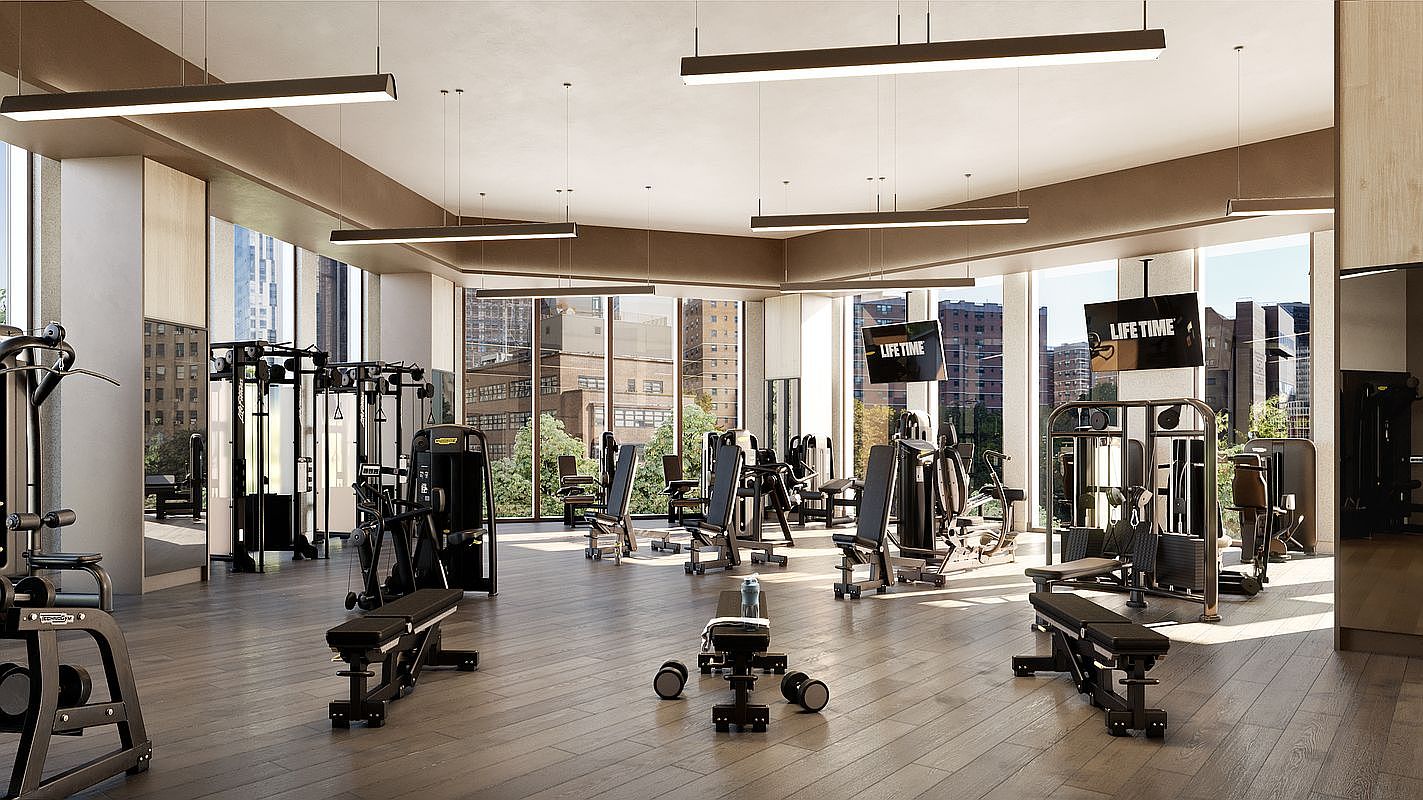 This professional-grade fitness center features a spacious, open-concept layout with high-end Technogym equipment and sleek, modern lighting fixtures. Large floor-to-ceiling windows provide an abundance of natural light and expansive city views, creating an inviting and upscale workout environment. The room is finished with warm wood-toned flooring, giving the space a sophisticated and polished aesthetic.