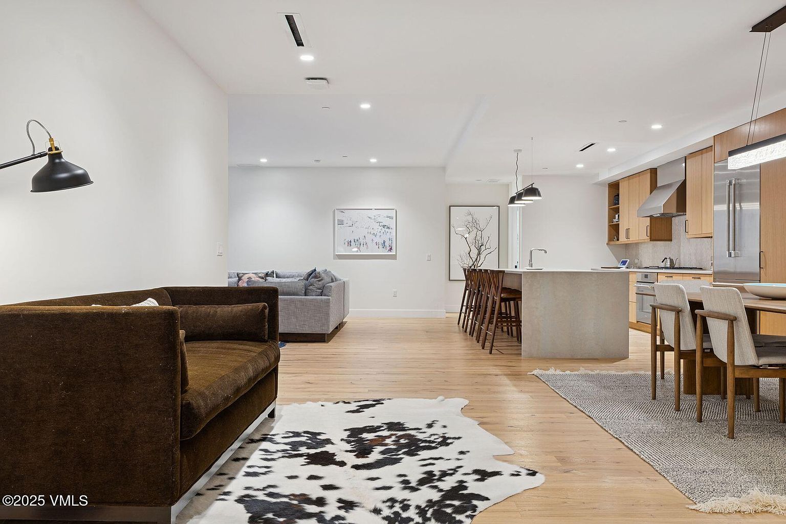 This interior shot showcases an open-concept living space that seamlessly integrates the living room, dining area, and kitchen. The living room features a brown sofa and a cowhide rug, while the dining area includes a wooden table with modern chairs. The kitchen boasts light wood cabinetry and a concrete island, creating a cohesive and stylish environment.