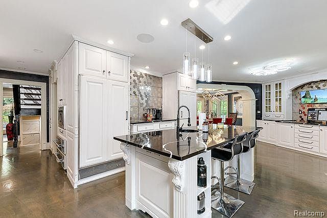 This is a bright and spacious kitchen featuring white cabinetry, a large center island with a black countertop, and stainless steel appliances. The kitchen is open to a dining area, creating a seamless flow for entertaining. The polished concrete floors add a modern touch to the space.