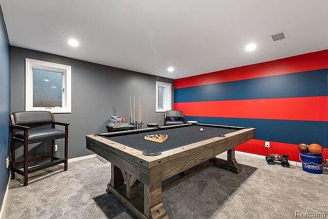 This is a finished basement featuring a pool table as the focal point. The walls are painted in a combination of gray and red/blue stripes, adding a playful touch. The room is well-lit with recessed lighting and includes a small window, creating a comfortable and inviting recreational space.