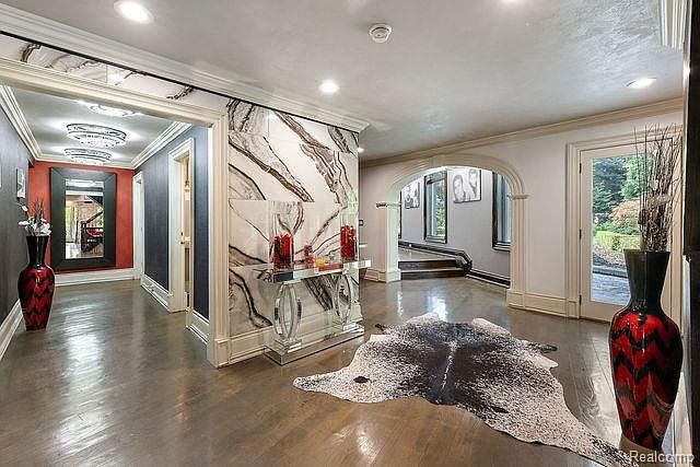 This interior shot showcases a grand hallway with hardwood floors, marble accent walls, and elegant lighting. A decorative cowhide rug adds a touch of modern flair, while doorways lead to other rooms, suggesting a spacious and well-designed home. The overall impression is luxurious and inviting.
