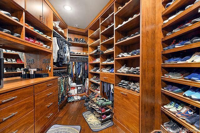 This is a well-organized walk-in closet featuring custom wooden shelving and drawers. The closet is filled with clothing, shoes, and accessories, showcasing ample storage space. The overall impression is luxurious and functional, highlighting the home's attention to detail and organization.