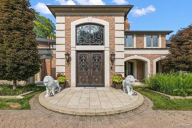 This image showcases the grand entryway of a brick home, featuring an ornate double door and a decorative window above. Two lion statues flank the entrance, adding a touch of elegance and grandeur. The paved walkway leads to the door, creating a welcoming and impressive approach to the property.