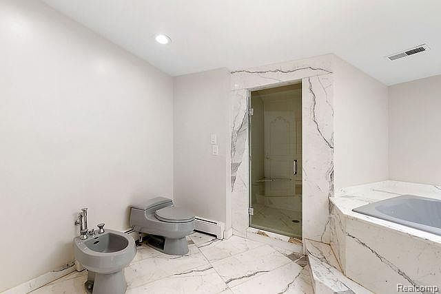 This primary bathroom features a modern design with marble flooring and walls. A glass-enclosed shower is adjacent to a large soaking tub with marble surround. A bidet and toilet are also visible, contributing to the luxurious feel of the space.