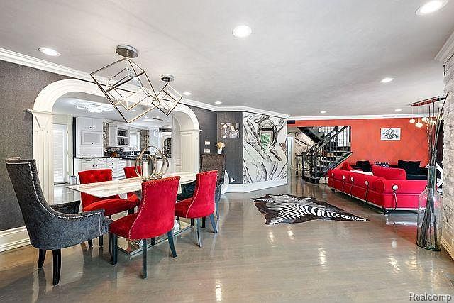 This interior shot showcases a modern dining area that seamlessly transitions into a living space. The dining area features a marble-top table surrounded by red velvet chairs and a unique geometric chandelier, while the adjacent living area boasts a vibrant red sofa and a zebra-print rug, creating a bold and eclectic aesthetic. The open floor plan and artistic wall decor contribute to a spacious and stylish atmosphere.