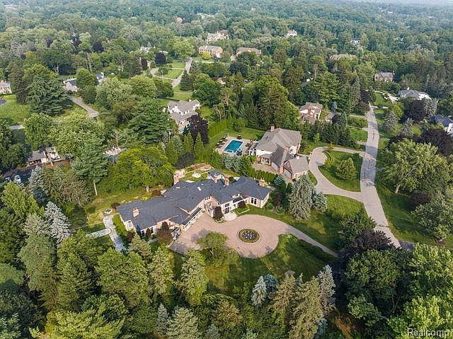 This aerial view showcases a sprawling estate nestled among lush greenery. The property features a large, well-maintained house with a circular driveway, a swimming pool, and mature trees providing privacy. The overall impression is one of luxury and seclusion, highlighting the expansive grounds and desirable location.