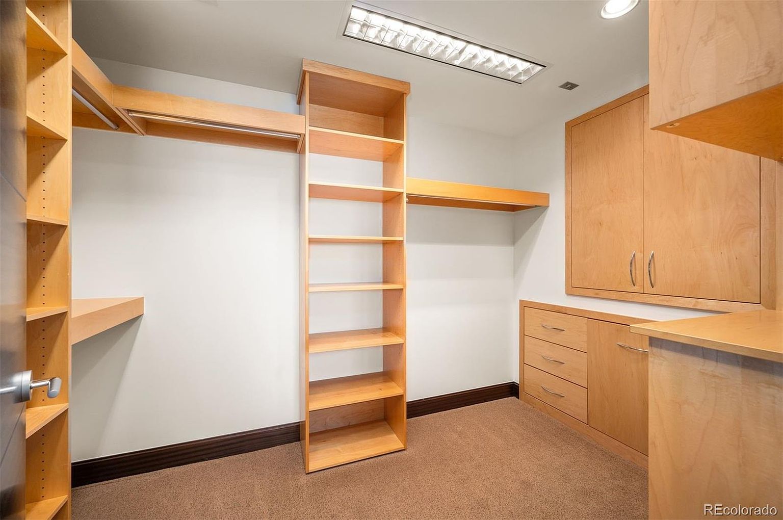 This is a well-organized walk-in closet featuring custom wooden shelving and cabinetry. The closet includes hanging rods, multiple shelves, and drawers, providing ample storage space. The neutral color palette and recessed lighting create a clean and functional space.