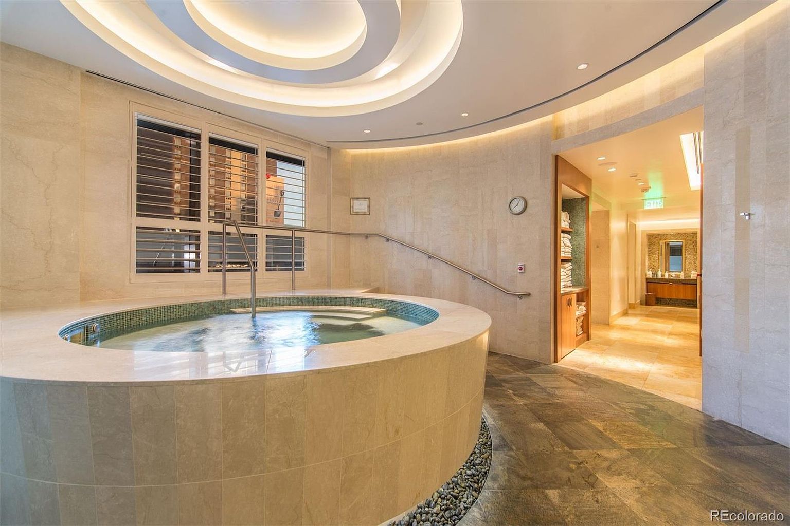 This image showcases a luxurious indoor spa area, featuring a circular hot tub with a tiled exterior and clear water. Natural light streams in through the window, complemented by the soft, ambient lighting from the ceiling. The space exudes a sense of relaxation and high-end comfort, making it an appealing amenity for potential buyers.
