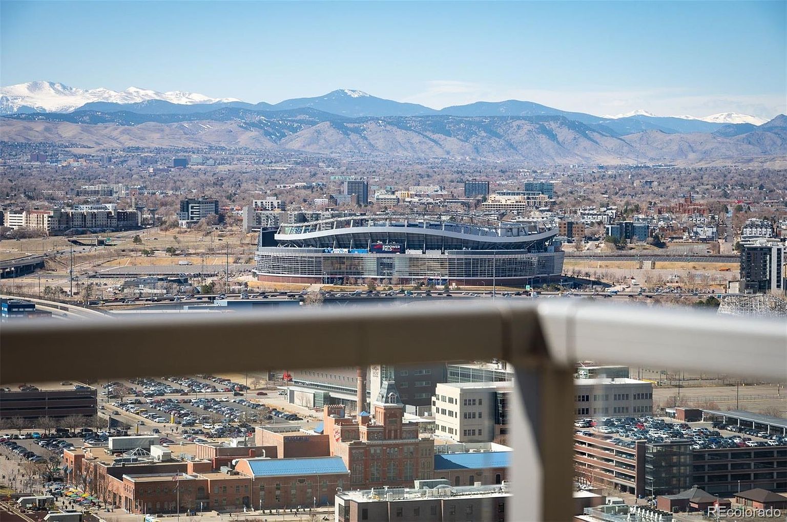 This aerial view showcases a sprawling cityscape with a prominent stadium in the foreground, set against a backdrop of majestic snow-capped mountains. The urban landscape features a mix of residential and commercial buildings, interspersed with green spaces, creating a dynamic and visually appealing scene. The image captures the scale and beauty of the city and its natural surroundings.