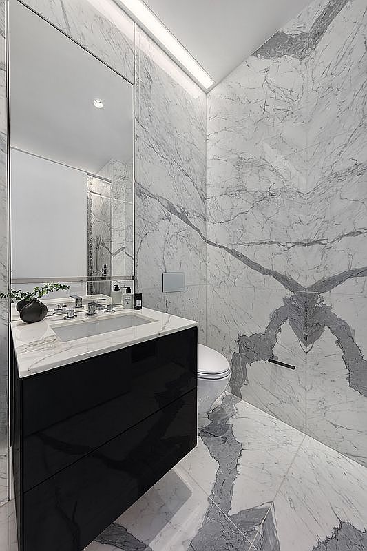 This sleek, modern powder room features dramatic, large-format marble wall and floor tiles with bold, dark veining. A high-gloss black vanity with a white marble countertop and integrated sink provides a striking contrast, while a tall, frameless mirror and recessed linear lighting enhance the sense of space. The minimalist design and high-end materials create a sophisticated and luxurious atmosphere.
