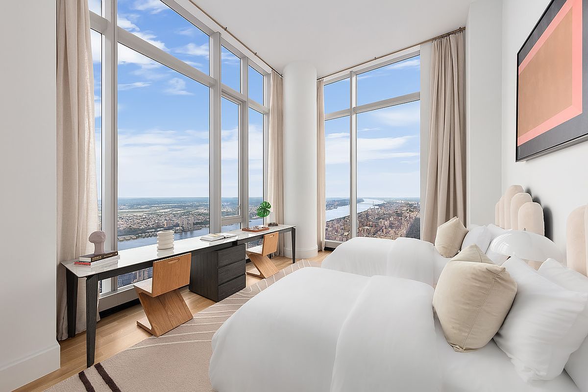 This sophisticated guest bedroom features two twin beds with crisp white linens and neutral-toned accent pillows, set against a backdrop of floor-to-ceiling windows offering a breathtaking, panoramic aerial view of the city and river. A sleek, modern desk runs along the window wall, paired with minimalist wooden chairs, creating a functional workspace that maximizes the stunning natural light. The room's clean lines, light color palette, and high-rise perspective evoke a sense of luxury, tranquility, and modern urban living.