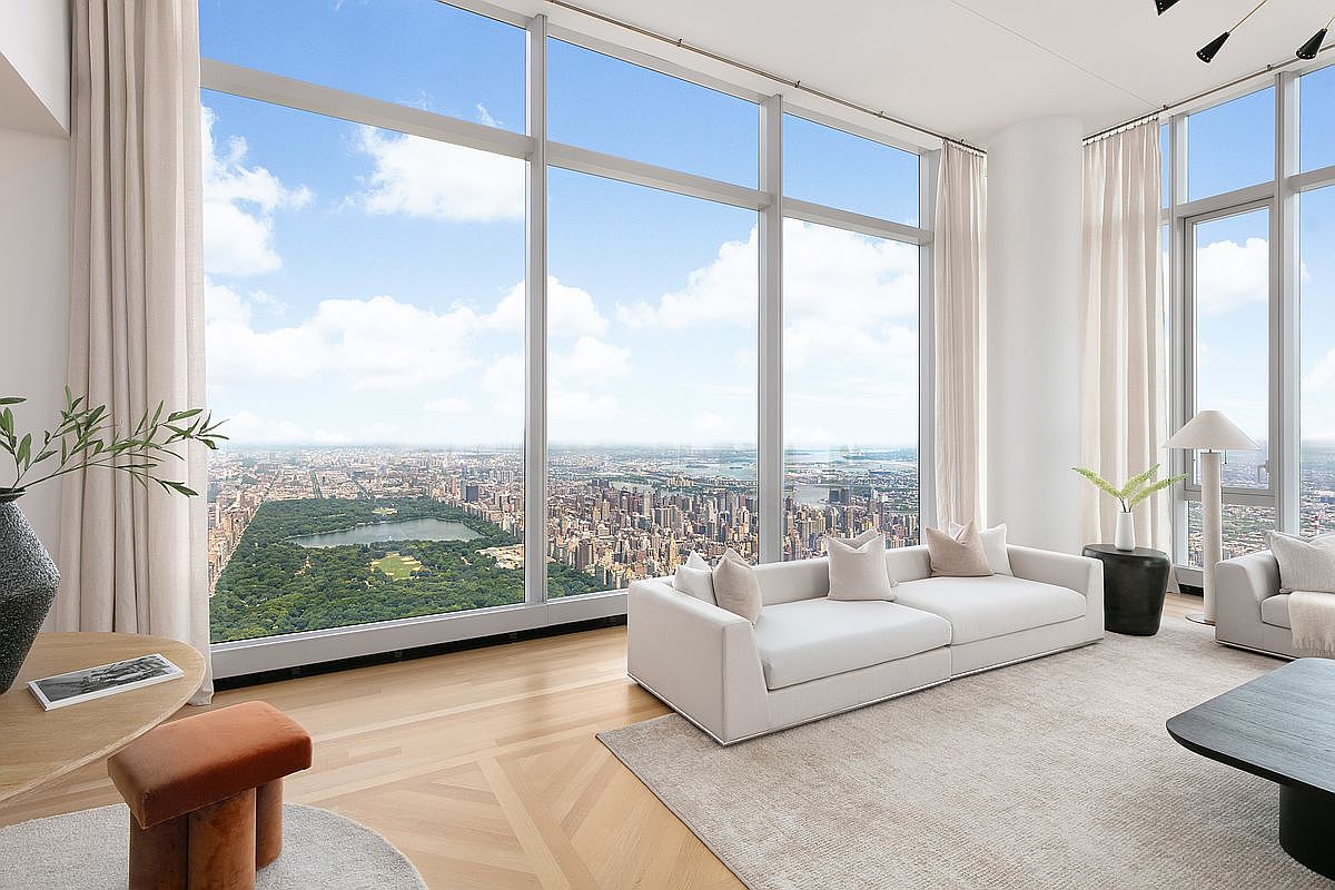 This sophisticated high-rise living room features floor-to-ceiling windows that offer a breathtaking, panoramic view of Central Park and the New York City skyline. The interior is elegantly furnished with a plush white sofa, a neutral area rug, and minimalist decor, creating a serene and luxurious atmosphere. The light wood flooring and soft, airy curtains enhance the bright, expansive feel of this premium urban residence.