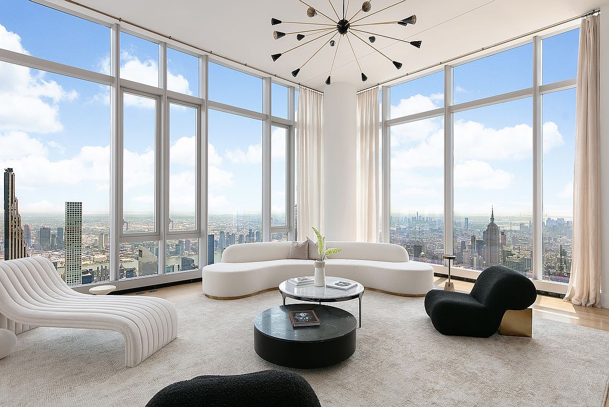 This luxurious, high-rise living room features floor-to-ceiling windows that offer a breathtaking, panoramic view of the city skyline. The space is anchored by a sophisticated, curved white sofa, a marble-topped coffee table, and a striking black sculptural chair, all set against a neutral, plush area rug. A modern, multi-armed sputnik-style chandelier hangs from the ceiling, adding a dramatic architectural element to this bright and airy contemporary living space.