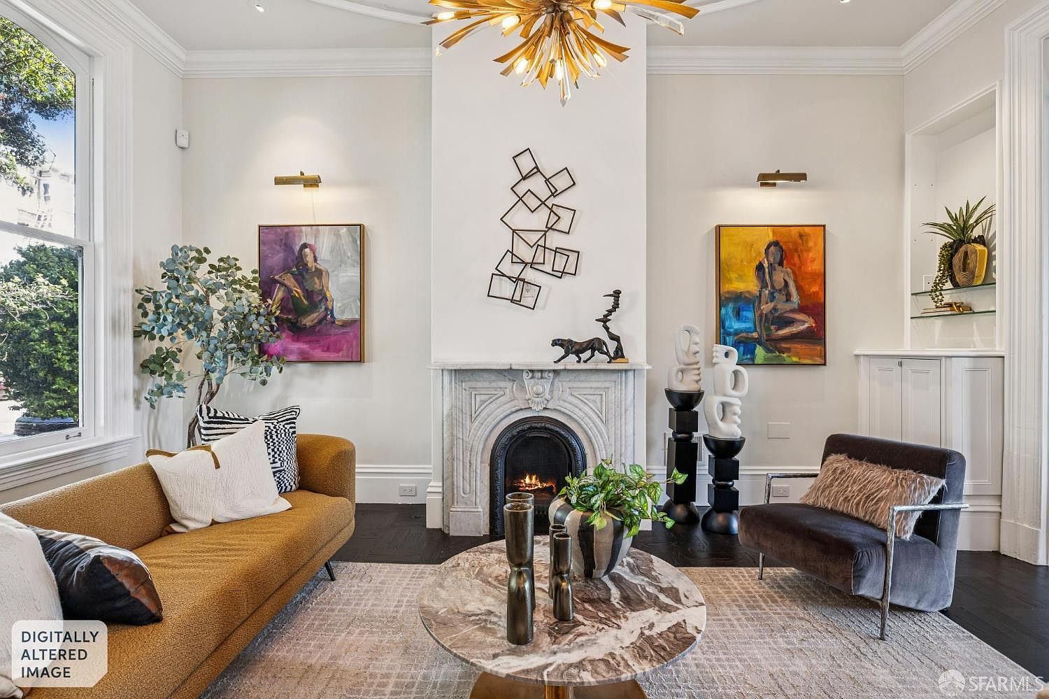 This elegant living room features a central fireplace with an ornate stone surround, flanked by two vibrant abstract paintings and wall-mounted accent lighting. A mustard-colored sofa and a dark velvet armchair are arranged around a circular stone-topped coffee table, all resting on a textured area rug. The space is anchored by a striking gold starburst chandelier and a geometric metal wall sculpture, creating a sophisticated and artistic atmosphere.