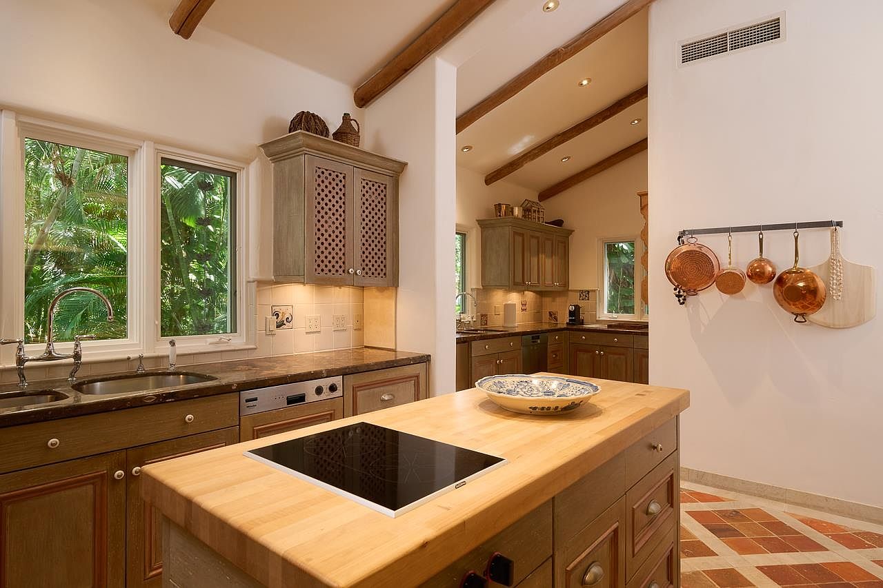 This is a warm and inviting kitchen featuring custom cabinetry with a unique lattice design on the upper cabinets. The kitchen island has a butcher block countertop and a built-in cooktop. Copper pots hang on the wall, adding a touch of rustic charm to the space.