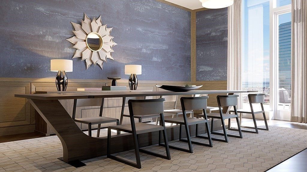 This sophisticated dining room features a long, modern wooden table paired with sleek, minimalist chairs, set against a textured, deep blue accent wall adorned with a striking sunburst mirror. The room is illuminated by soft, ambient lighting from table lamps and a large window that invites natural light, creating an atmosphere of refined elegance. The perspective is a wide, eye-level shot that emphasizes the clean lines and contemporary design of the space.