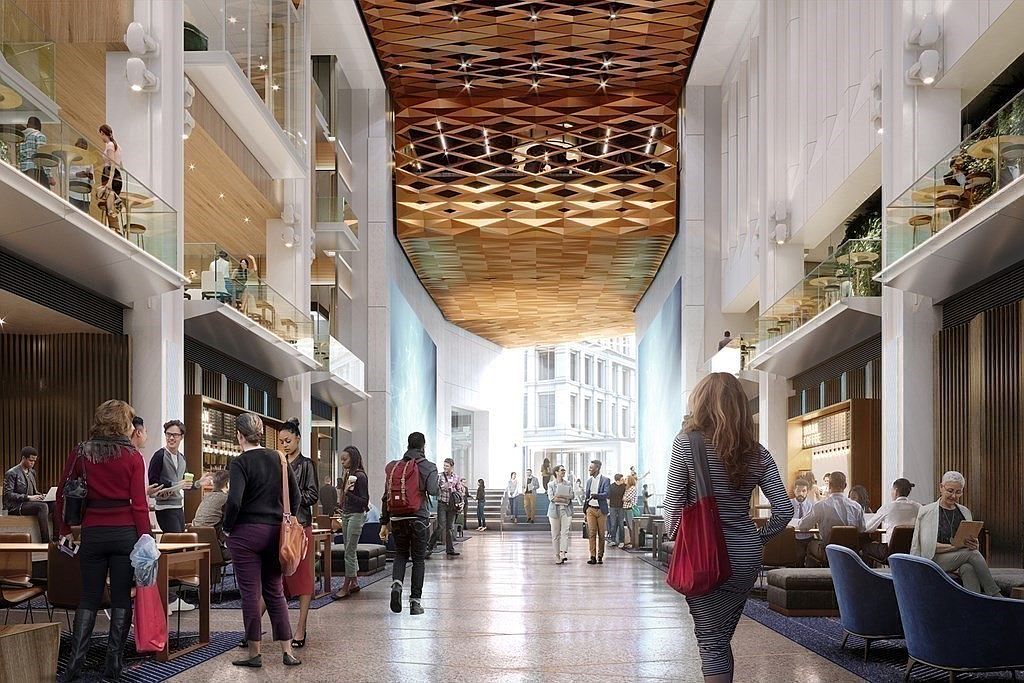This image depicts a sophisticated, multi-level atrium lobby or common area within a modern commercial or residential building. The space features a striking geometric wooden ceiling, polished stone flooring, and open-concept mezzanine levels with glass railings, creating an airy and upscale atmosphere. Numerous people are seen socializing, working, and walking through the bustling, light-filled corridor, which serves as a vibrant hub for community interaction.