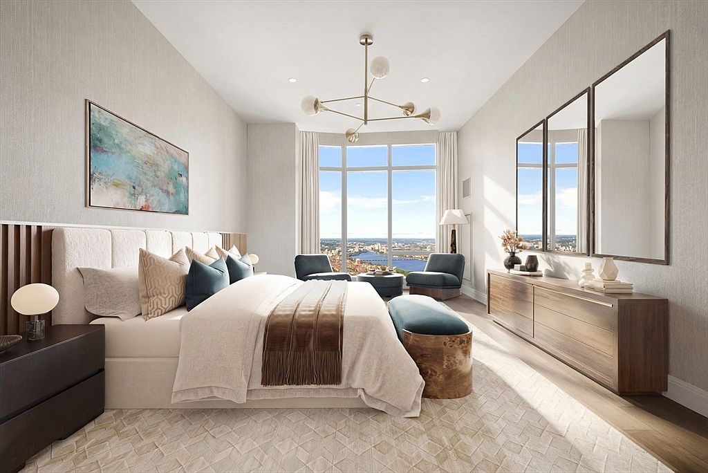 This luxurious primary bedroom features a sophisticated, neutral color palette with high-end finishes and a stunning floor-to-ceiling window offering panoramic city and water views. The room is anchored by a plush bed with layered textiles, a unique wooden-base bench, and a sleek, modern dresser topped with three large mirrors. The cinematic perspective captures the elegance of the space, highlighting the designer chandelier and the seamless blend of comfort and contemporary style.