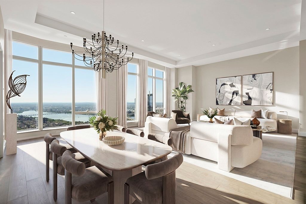 This sophisticated open-concept living and dining area features floor-to-ceiling windows that offer a breathtaking panoramic view of the city skyline and river. The space is elegantly furnished with plush, cream-colored sofas, a sleek dining table with upholstered chairs, and a striking modern chandelier, all set against a neutral, high-end color palette. The cinematic perspective captures the seamless blend of luxury interior design and the expansive natural light pouring in from the exterior.