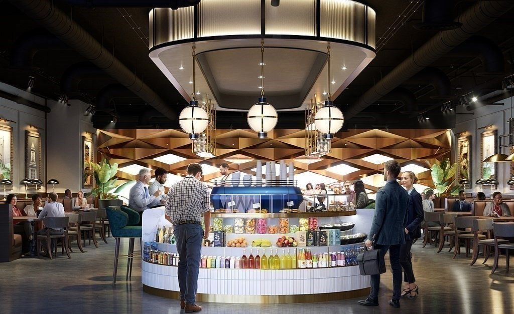 This sophisticated, modern cafe or lounge area serves as a high-end community amenity, featuring a central circular service counter stocked with refreshments and snacks. The space is defined by elegant geometric wall paneling, warm pendant lighting, and a polished, professional atmosphere with patrons socializing and working. The perspective is a wide, eye-level shot that captures the inviting, upscale ambiance of a shared commercial space.