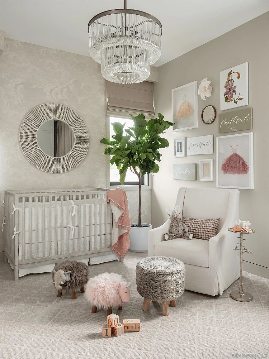 This is a charming nursery featuring a grey crib with white linens, complemented by decorative sheep and an elephant stool. A comfortable white armchair with a patterned pillow sits beside a woven ottoman and a small side table, creating a cozy and inviting atmosphere. The room is decorated with framed artwork and a round mirror, enhancing the room's aesthetic appeal.