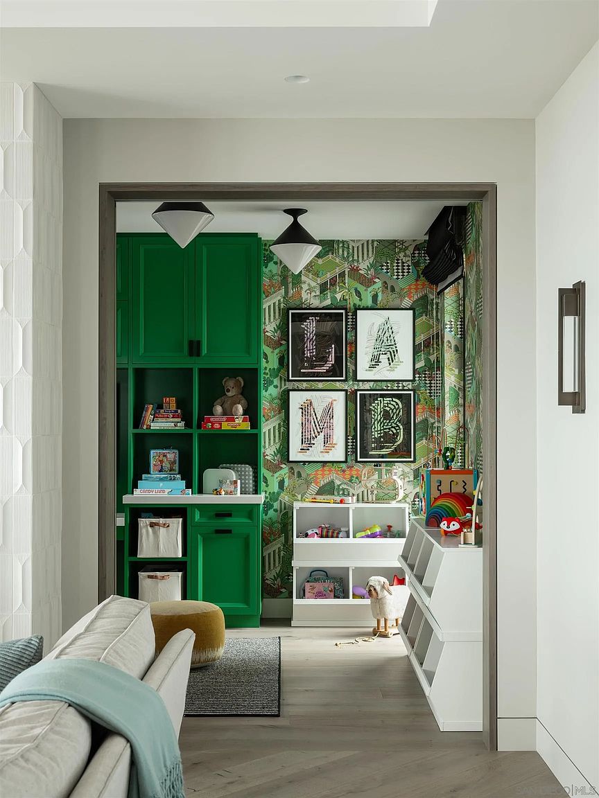 This is a charming children's room featuring vibrant green built-in shelving and playful wallpaper with a jungle theme. The room is well-organized with toys neatly arranged on shelves and in storage bins. The space is inviting and designed to stimulate creativity and play, making it an ideal space for children.