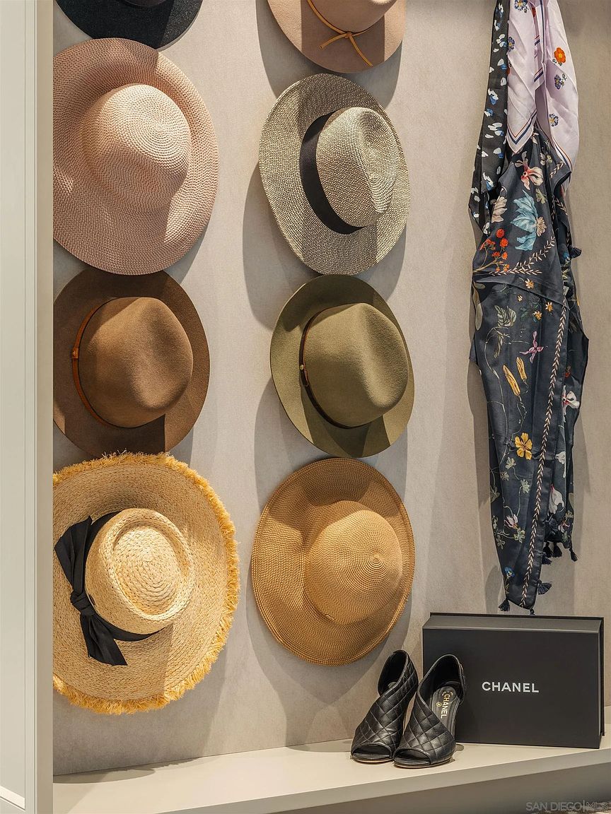 This image showcases a well-organized walk-in closet featuring a collection of hats displayed on the wall, along with a designer scarf, shoes, and a Chanel box on a shelf. The arrangement suggests a focus on fashion and luxury, highlighting the closet's potential for stylish storage and display. The perspective is a medium shot, emphasizing the curated collection.