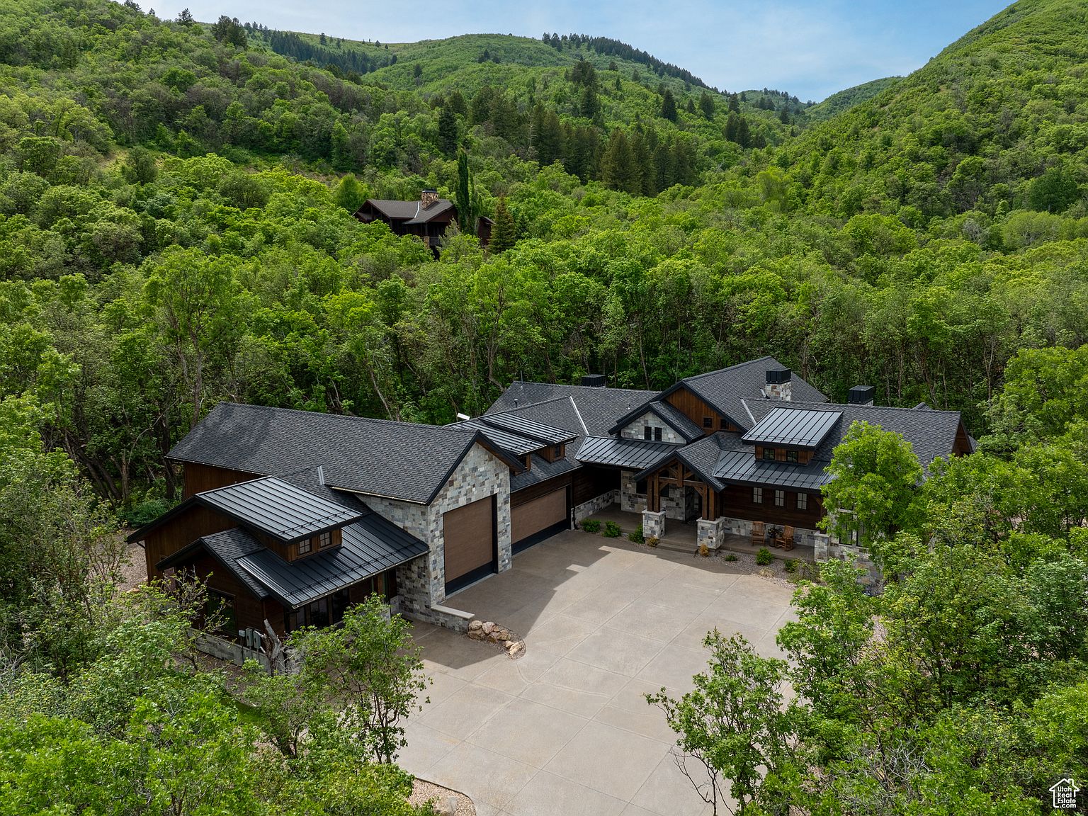 This aerial shot showcases a luxurious home nestled in a lush, green valley. The house features a dark roof, stone accents, and a spacious driveway. The surrounding trees provide privacy and a sense of seclusion, making it an ideal retreat.