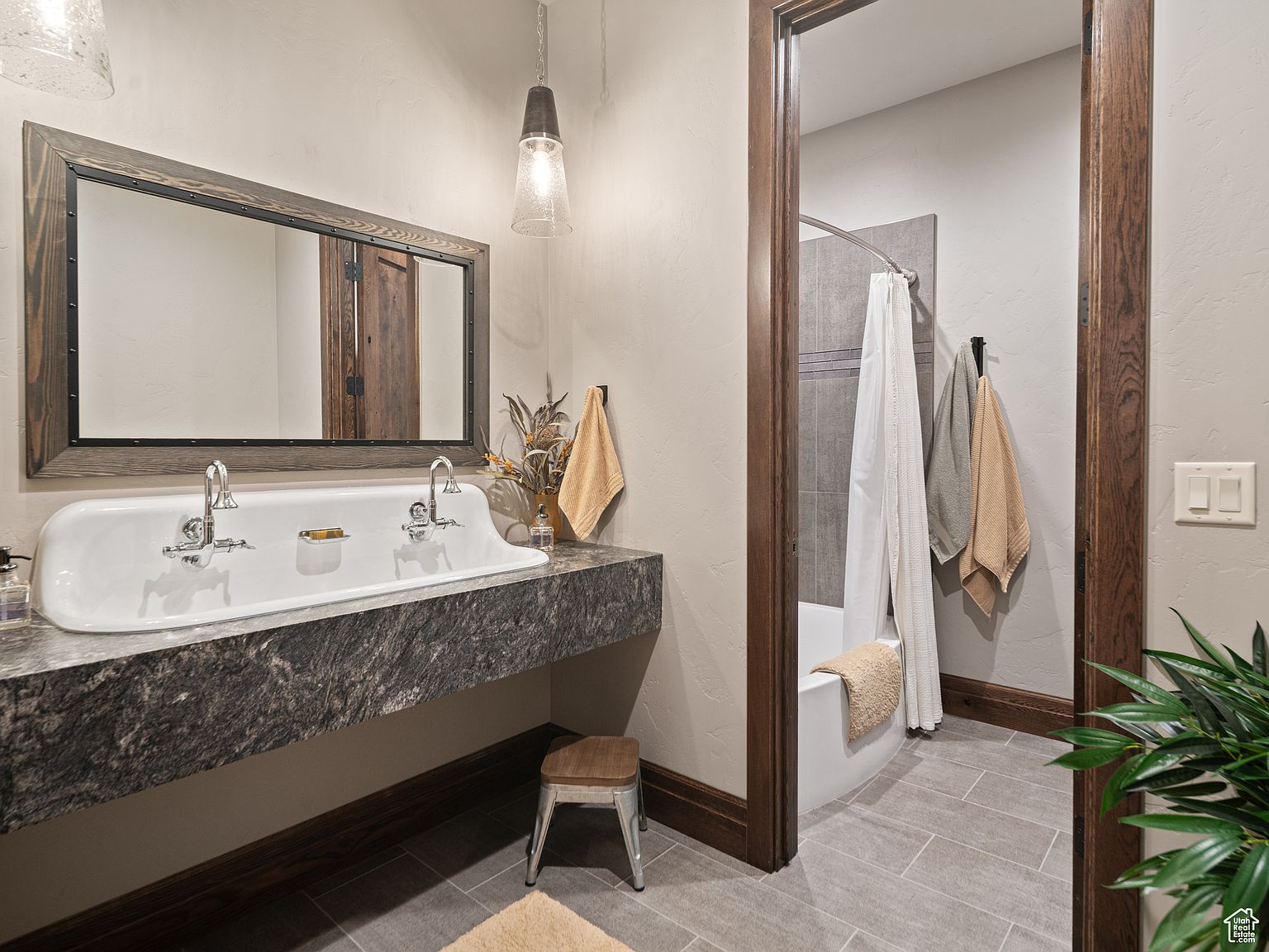 This is a well-appointed guest bathroom featuring a unique double sink with a dark granite countertop and a wood-framed mirror. The bathroom includes a separate shower/tub area visible through a wood-framed doorway, enhancing the room's rustic yet elegant style. The neutral wall color and wood trim create a warm and inviting atmosphere.