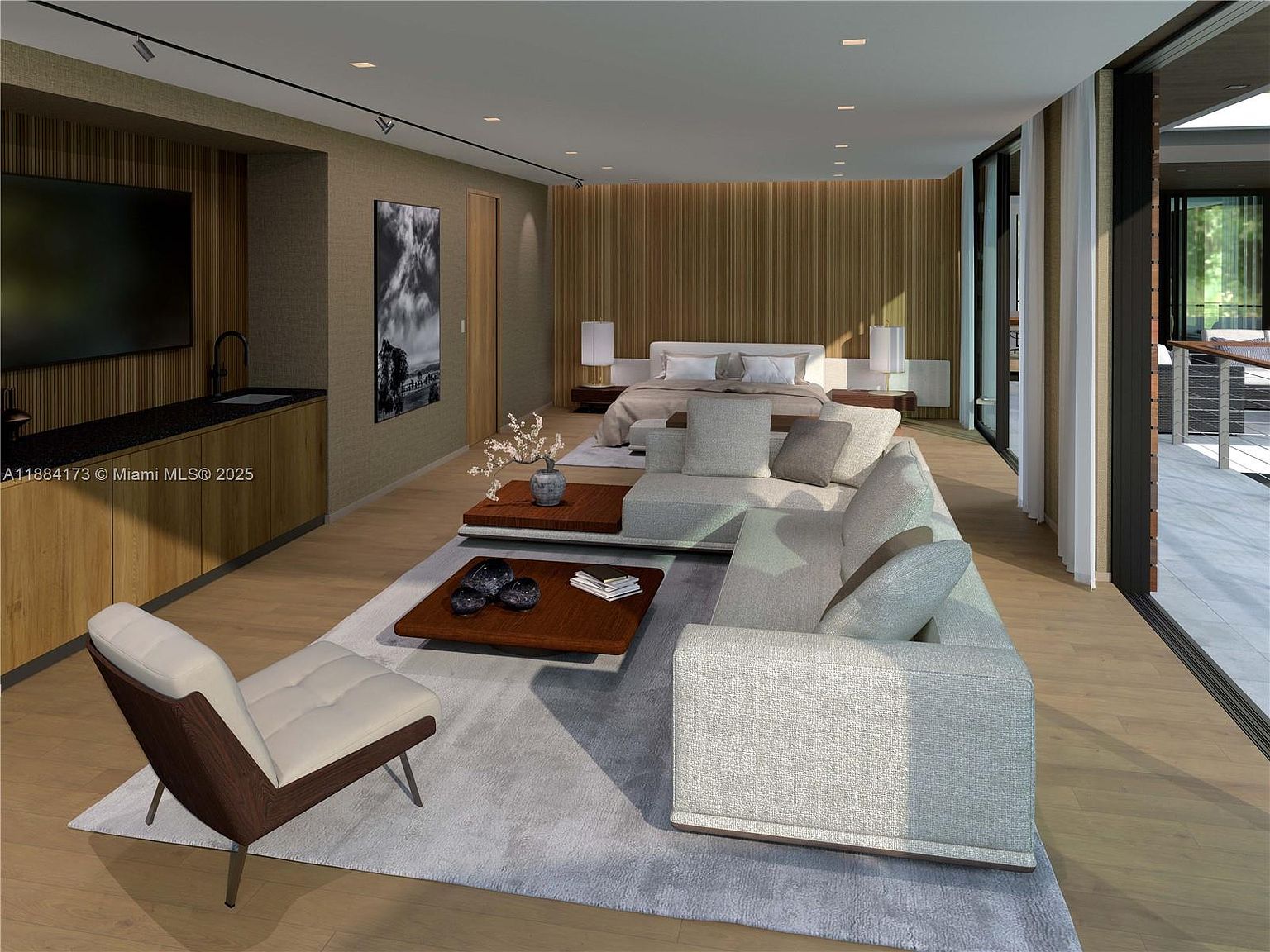 This is a spacious primary bedroom featuring a modern design with a large bed, a seating area with a sectional sofa, and a dark wood accent wall. The room has a light color palette with wood flooring and a large area rug. The perspective is from the side of the room, showing the bed and seating area.