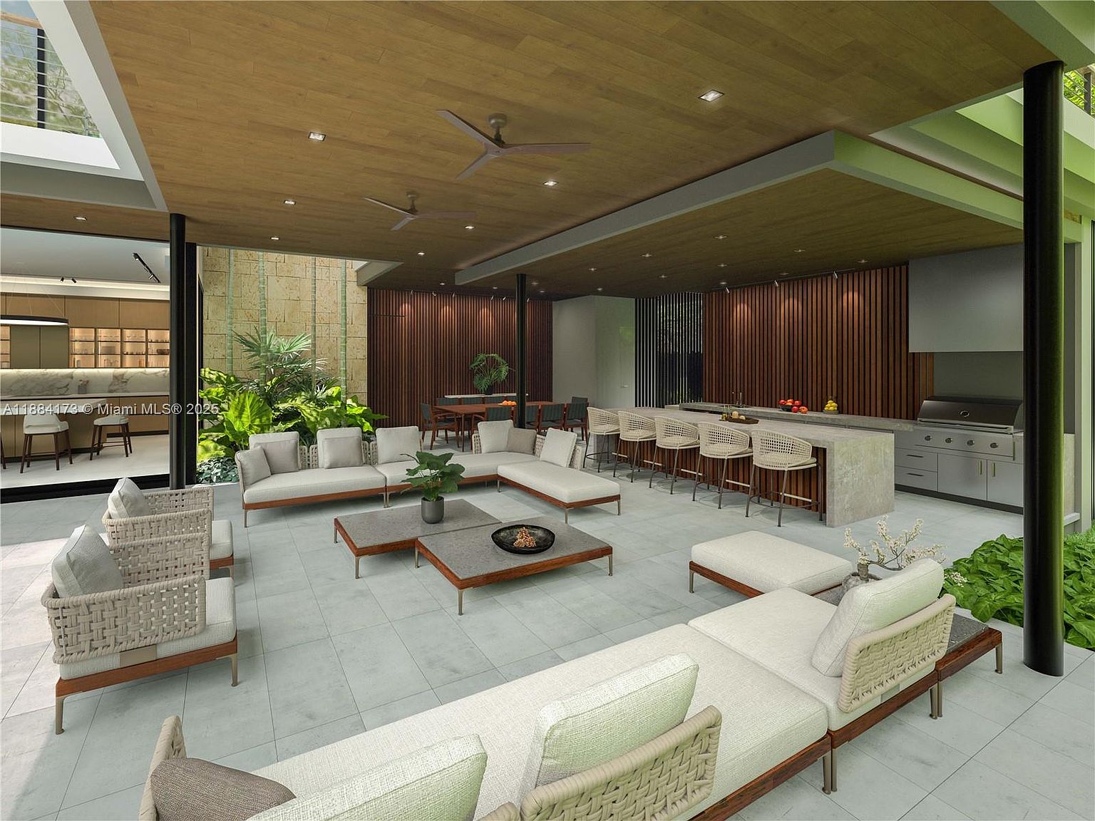 This image showcases a luxurious outdoor living space, featuring multiple seating areas with modern, woven-style furniture and sleek coffee tables. The space is partially covered by a wooden ceiling with ceiling fans, and includes an outdoor kitchen area with a grill and bar seating. Lush greenery surrounds the patio, creating a serene and inviting atmosphere.
