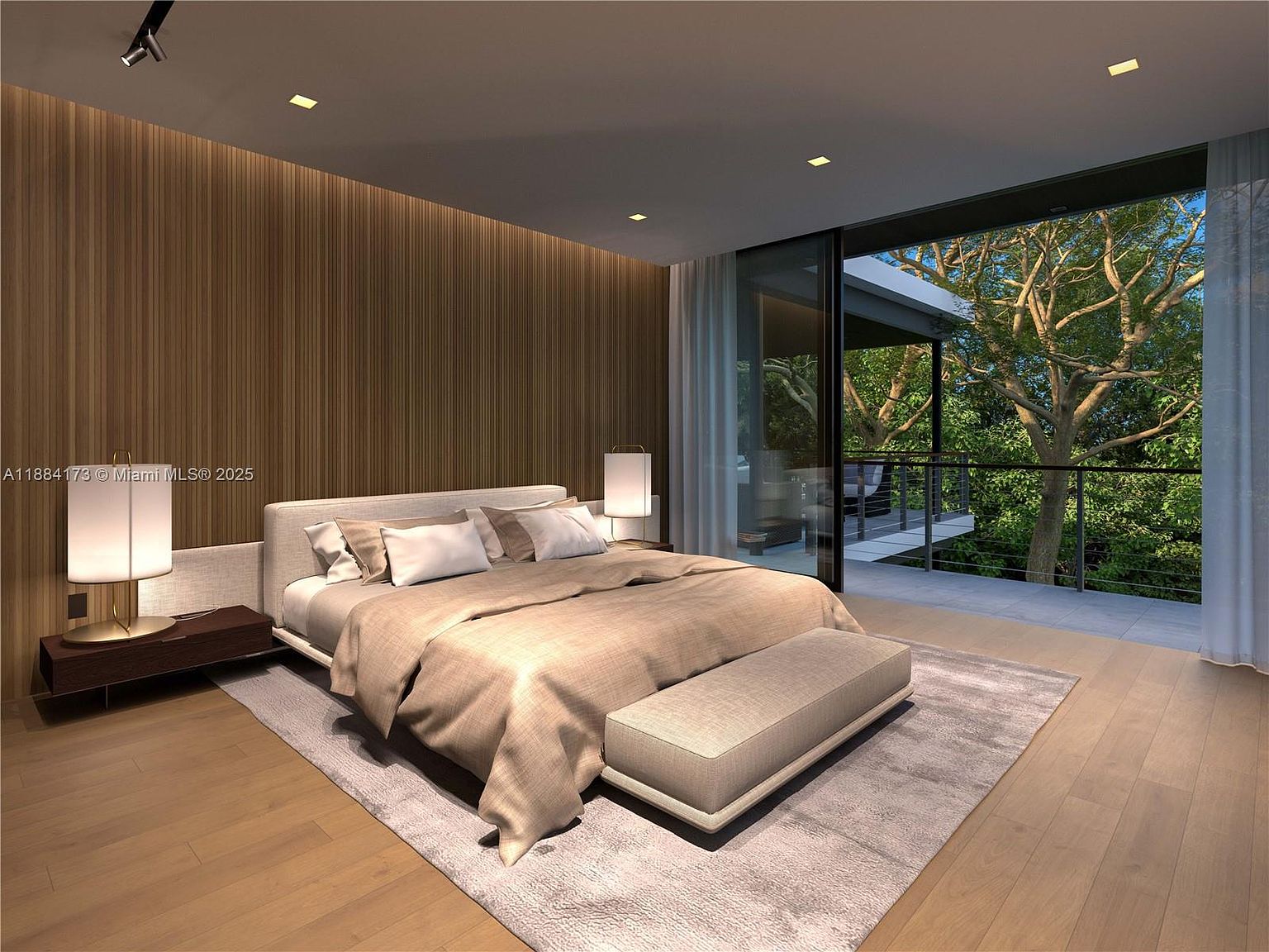 This is a luxurious primary bedroom featuring a large bed with neutral-toned linens, a bench at the foot of the bed, and a textured rug. The room has a modern aesthetic with a wood-paneled accent wall and floor-to-ceiling windows that open to a balcony overlooking lush greenery, creating a serene and inviting atmosphere.