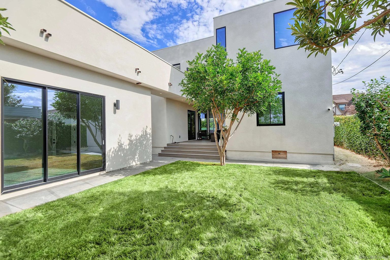 This image showcases the rear exterior of a modern home, emphasizing the well-maintained yard. A vibrant green lawn extends from the building, complemented by a neatly trimmed tree. The architectural style is contemporary, with clean lines and large windows, creating an inviting outdoor space.